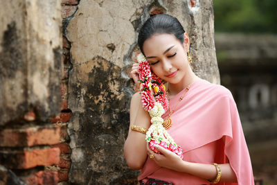 Young woman wearing sari holding floral garland by wall