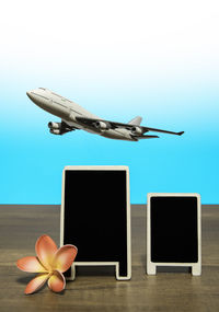 Close-up of airplane over blank blackboards and flower on wooden table against colored background