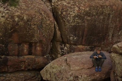 High angle view of man reading book while sitting on rock