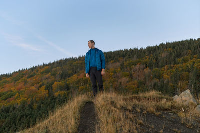 Low angle view of man standing on ridge against forest