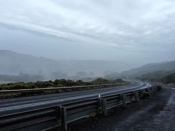 Road passing through mountains against cloudy sky