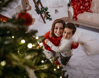 Single mother and her little son embracing and looking camera with pleasant smile at cozy home