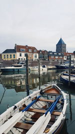 Boats moored in river by buildings in city against sky