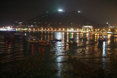 Illuminated city by sea against sky at night