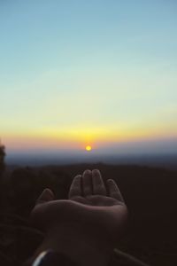 Hand of person against sky during sunset