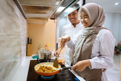 Young woman holding food while standing at kitchen