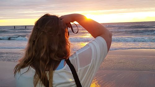 Rear view of woman standing at beach during sunset