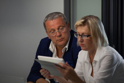 Serious mature couple wearing eyeglasses while looking at digital tablet in room