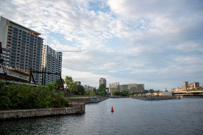 City buildings by river against sky