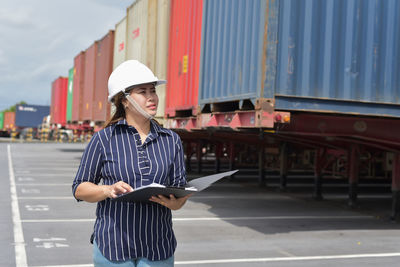 Female engineer holding file while standing by cargo container