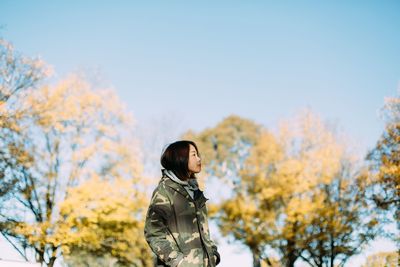 Woman in warm clothes standing against trees 