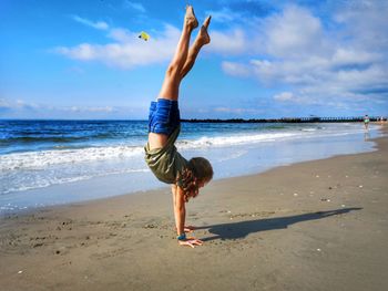 Girl doing handstand at beach against sky