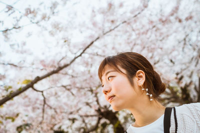 Portrait of young woman looking at cherry blossom