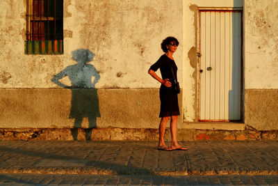 Woman standing against house during sunset