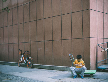Man sitting on bicycle against wall in city