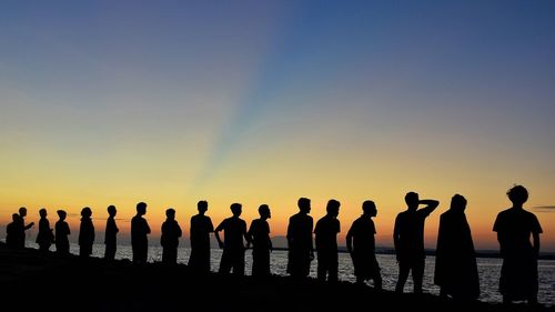 Silhouette people standing by sea against sky during sunset