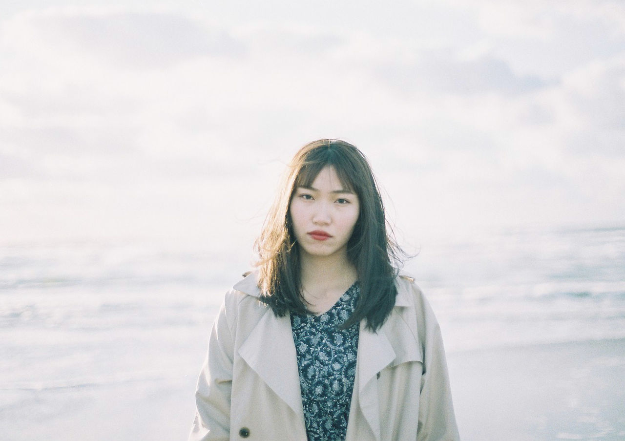 PORTRAIT OF YOUNG WOMAN STANDING AGAINST SEA