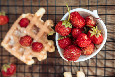 Fresh strawberries in a bowl and with viennese waffles on a wooden table top view