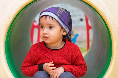 Cute girl looking away while sitting on outdoor play equipment