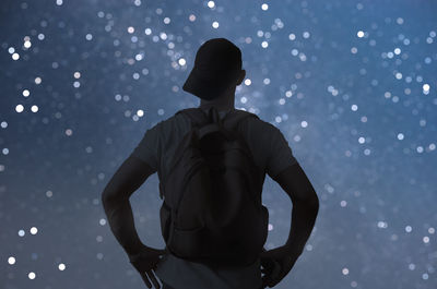 Rear view of silhouette man standing against illuminated light