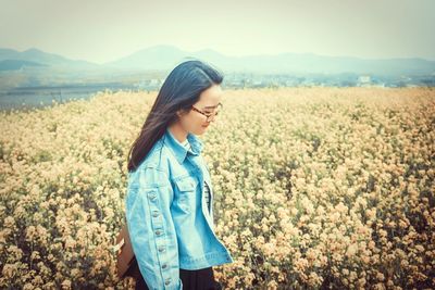 Young woman standing on field against sky