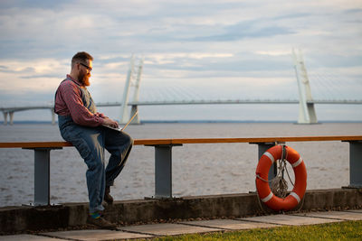 Bearded man freelancer working on laptop at embankment outdoors. distance job, remote work.