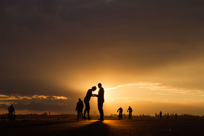 Silhouette people on street against orange sky