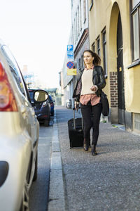 Businesswoman with luggage walking towards car parked on street