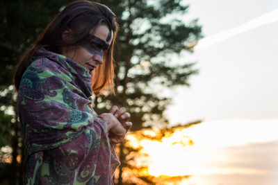 Side view of woman with black face paint wrapped in blanket during sunset