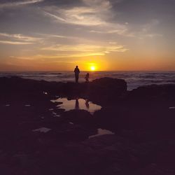 Silhouette man standing on beach against sky during sunset