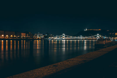 Illuminated bridge over river against sky at night