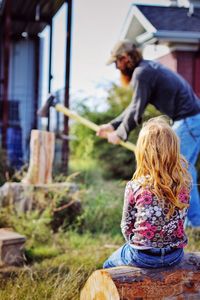 Girl looking at father cutting wood with axe on grassy field