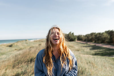 Cheerful young female in casual outfit standing on grassy meadow in summer with eyes closed