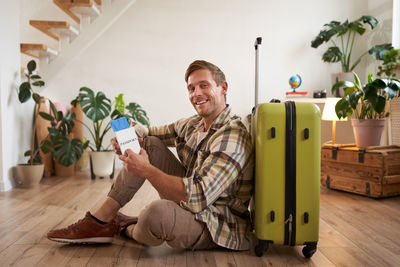 Portrait of young woman sitting on suitcase at home