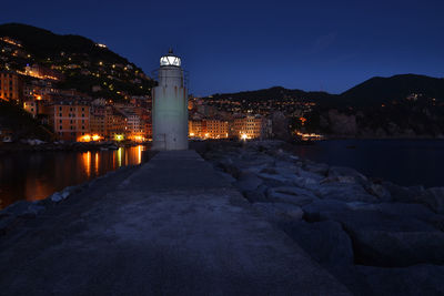 Illuminated buildings by sea against sky at night