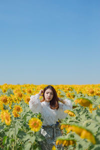 Young woman with yellow flowers on land against clear sky