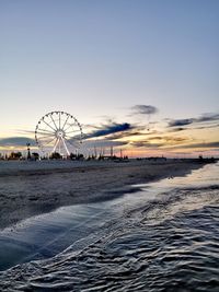 Ferris wheel on beach against sky during sunset