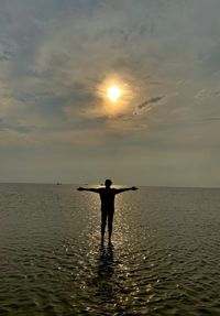 Rear view of silhouette man standing on sea against sky during sunset
