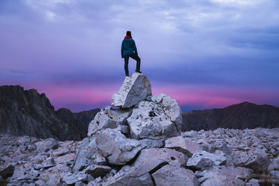 Rear view of woman standing on rocks against sky at dusk