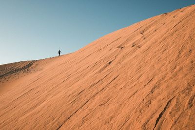 Low angle view of young woman standing on sand dune against clear sky