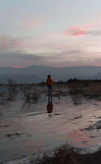 Silhouette man standing on shore against sky during sunset