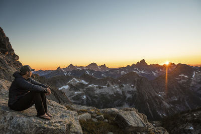 Active fit man resting on rock in mountains watching sunset.