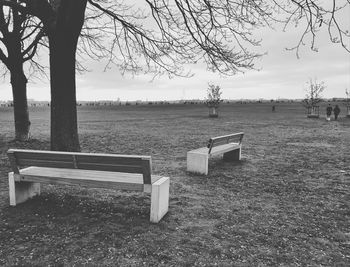 Empty bench on field against sky