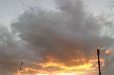 Low angle view of electricity pylon against cloudy sky