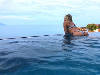 Woman sitting in swimming pool against sea