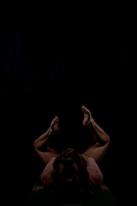 Midsection of young woman with arms raised against black background