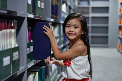 Smiling girl keeping book in shelf at library