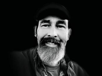 Close-up portrait of smiling mature man against black background