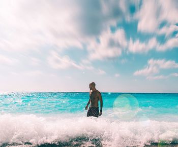 Shirtless man standing in sea against sky on sunny day