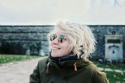 Portrait of smiling young woman wearing sunglasses against sky
